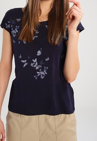 Camiseta de algodón azul marino con un patrón de mariposas en tonos más claros, con cuello redondo y mangas cortas.