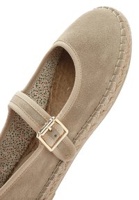 Bailarinas de ante beige con una correa al tobillo, suela de yute trenzado y plantilla con un diseño. Cuenta con una pequeña hebilla dorada en la correa ajustable.