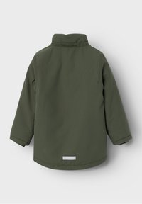 Chaqueta de tela verde con cuello alzado, mangas largas y un logo reflectante en la parte trasera. Textura suave, diseño minimalista sin características adicionales.