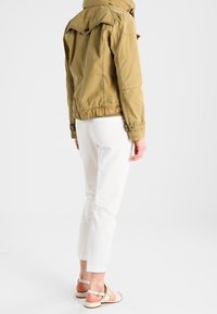 Grön bomulljacka med huva, samlad midja och knapprar. Kombinerad med vita åtsittande byxor och beige sandaler med rem.