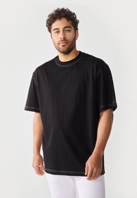 Sort kortærmet t-shirt med rund hals, der har kontrastfarvet hvid søm. Stoffet ser blødt ud med en løs og afslappet pasform.
