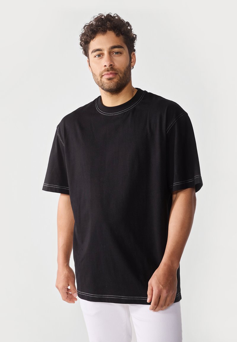 Svart kortermet t-skjorte med rund hals, med kontrasterende hvit søm. Stoffet ser mykt ut med en løs og avslappet passform.