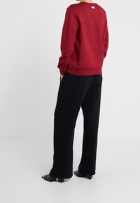 Röd sweatshirt med logotyp på ryggen, kombinerad med svarta vida byxor. Outfiten har en avslappnad passform och enhetliga färger.