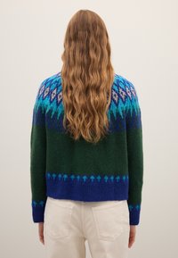 Strickpullover in Dunkelgrün mit einem blauen und türkisfarbenen Fair-Isle-Muster auf den Schultern und einer strukturierten Oberfläche. Cropped-Länge.