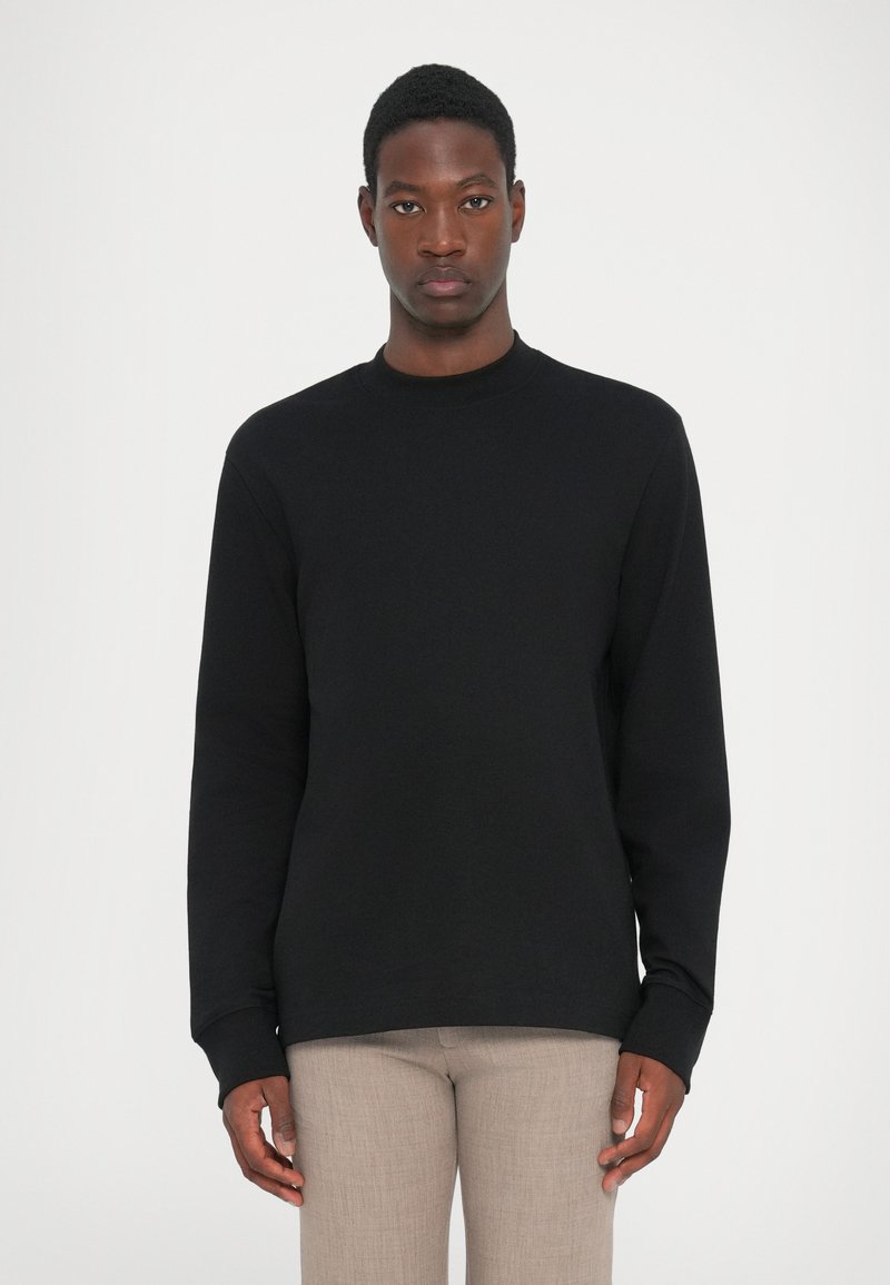 Svart långärmad sweatshirt med rund halsringning. Slät bomullstyg, åtsittande muddar och en avslappnad silhuett. Enkelt mönster, inga mönster.