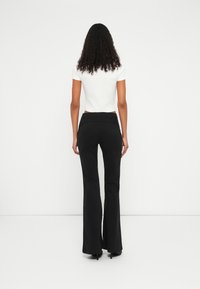 Pantalones acampanados negros con una cintura alta, combinados con una blusa ajustada de manga corta blanca. Tejido suave con un diseño clásico.