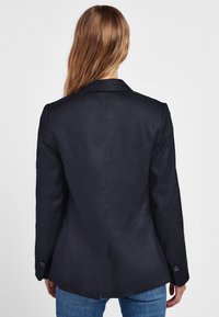 Granatowa marynarka o prostym kroju, z pojedynczym rozcięciem z tyłu i mankietami zapinanymi na guziki. Wykonana z gładkiej tkaniny, o dopasowanym kroju.