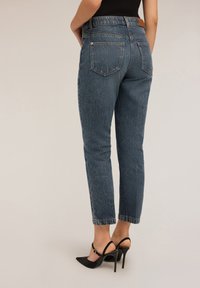 Jeans oscuros de cintura alta con un corte recto, que cuentan con bolsillos traseros y ligeras arrugas; combinados con unos tacones negros de punta.