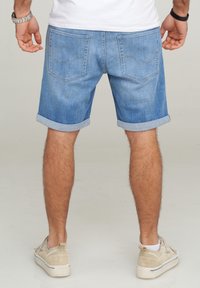 Shorts de mezclilla azul claro con puños enrollados, que cuentan con dos bolsillos traseros y detalles de costura sutiles. Llevados con zapatillas casuales beige.