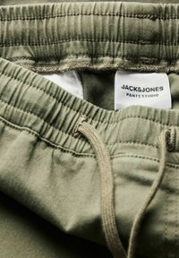 Pantalon à taille élastique vert olive avec cordon de serrage et étiquette blanche visible Jack & Jones Pants Studio à l’intérieur.