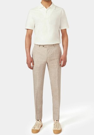 Herenoutfit met een lichtbeige linnen polohemd, lichtbeige op maat gemaakte broek en crèmekleurige sneakers met gestructureerde zolen.