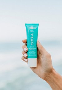 Turkusowa tuba przeciwsłonecznego kremu do twarzy Coola Classic; 70% organiczny; tekst zawiera "Biała herbata", "SPF 50" oraz "Wodoodporny". Pojemność 60 ml.