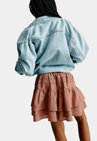 Ljusblå denimjacka med oversized passform, tillsammans med en lager-på-lager dammig rosa kjol med ögonfransdetaljer och volangkant.