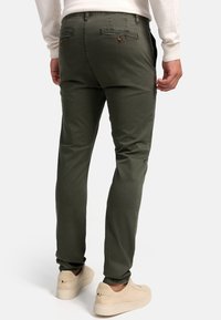 Pantalones slim-fit en verde oliva con un sutil patrón texturizado. Cuentan con bolsillos frontales inclinados y un detalle de costura en contraste en la parte trasera.