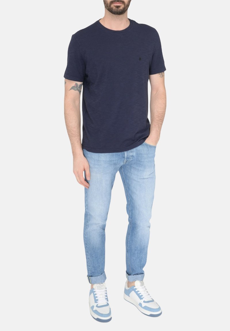 T-shirt girocollo blu navy, vestibilità casual, texture morbida. Abbinato a jeans in denim blu chiaro e sneakers con dettagli blu.