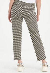 Černobílé kostičkované kalhoty slim fit. Obsahují dvě zadní kapsy a lem mírně nad kotníky, doplněné o světlé tenisky.