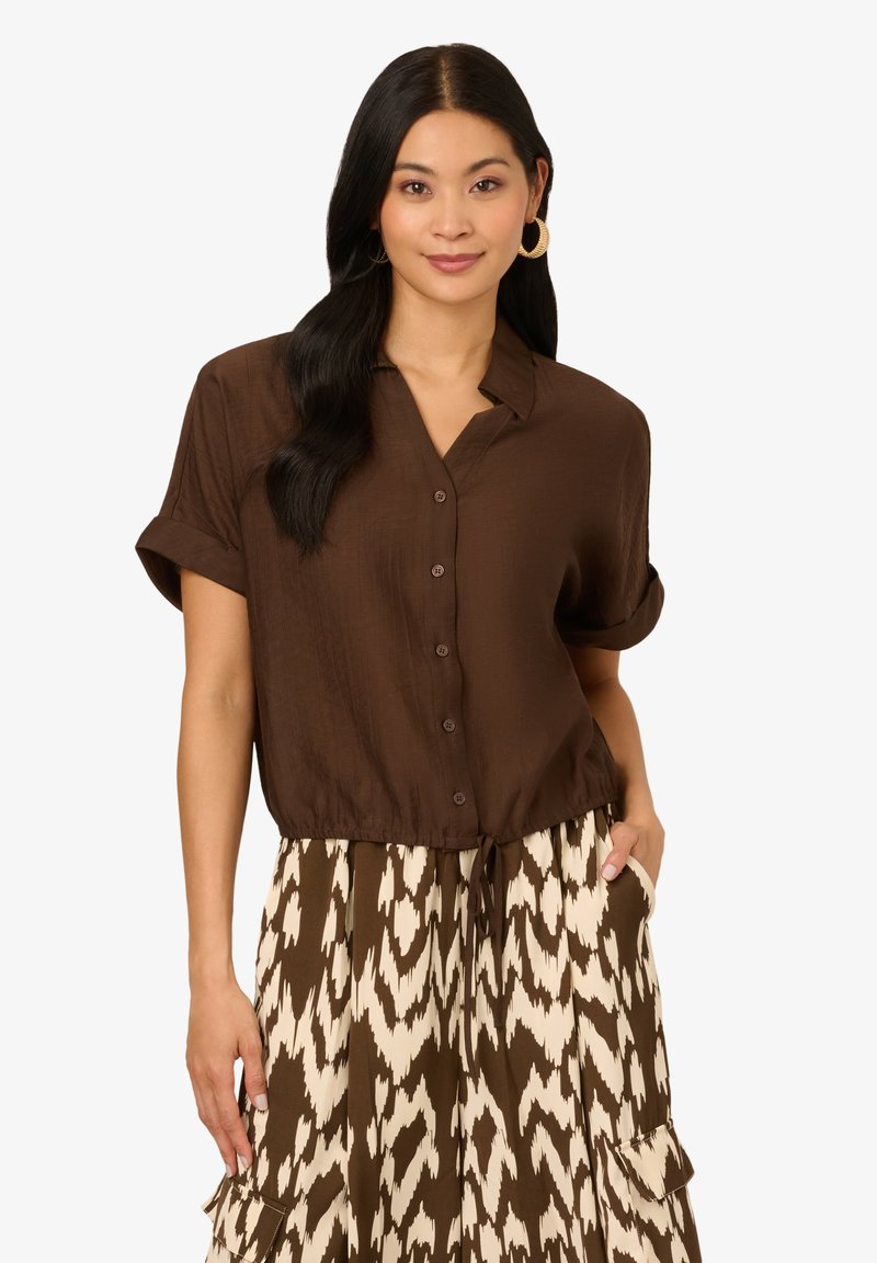 Chemise brune à manches courtes avec col, associée à une jupe motif crème et brun avec taille élastique et poches.
