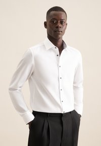 Witte lange mouwen overhemd met een contrasterende kraag, knoopsluiting aan de voorkant en grijze knoopaccenten, gecombineerd met zwarte broek.