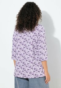 Fioletowo-biała bluzka w długa wzory z okrągłym dekoltem i rękawami do łokcia; tkanina ma gładką fakturę, lekko luźny krój.