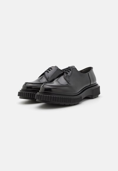 Schwarze Lackleder-Schuhe mit abgerundetem Zehenbereich, ausgestattet mit einer dicken geriffelten Sohle und Schnürdesign. Glatte Textur mit minimalen Nähdetails.