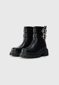 Black leather ankle boots with chunky soles, double silver buckle straps, and a pull tab at the back, shown on a plain white background.