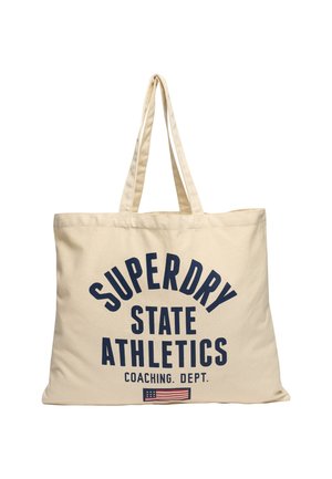 Sac fourre-tout beige avec deux poignées, texte bleu "Superdry State Athletics Coaching Dept." et un petit graphique du drapeau américain en bas au centre.