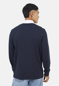 Camicia a maniche lunghe blu navy con colletto bianco. Design semplice, texture morbida e vestibilità regolare. La vista posteriore mostra la lunghezza della camicia e il dettaglio delle maniche.