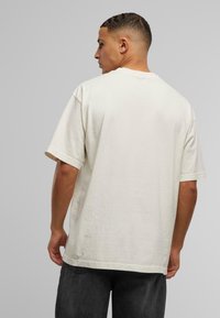 Unisex oversized cremet T-shirt i bomuld med korte ærmer, rund hals og afslappet pasform. Glat tekstur; ingen synlige mønstre eller accenter.