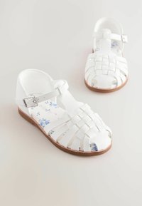 Weiße Ledersandalen mit geflochtenem Design, verstellbarem Knöchelriemen und floral bedruckter Innensohle. Flache braune Sohle. Strapazierfähig und atmungsaktiv.