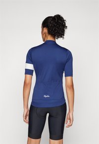 Marineblaue Radtrikot mit kurzen Ärmeln, ausgestattet mit einem weißen Streifen am linken Arm und einem Signatur-Logo auf der Rückseite. Strukturiertes, eng anliegendes Design.