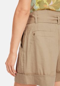 Beige linen shorts featuring a wide waistband, side pockets, and a single back pocket with a silver snap closure.