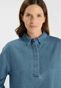 Denim shirt in een middelblauwe tint met een knoopsluiting en een kraag. Bevat subtiele diagonale stiksels en een gestructureerde afwerking.