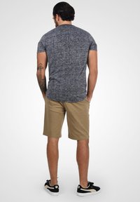 Grå meleret kortærmet skjorte, beige shorts og sorte sneakers med hvide såler. Synlig tatovering på venstre arm.