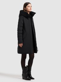 Melnā polsterētā virsjaka ar lielu kapuci, priekšējo rāvējslēdzēju un sānu kabatām. Raksturīga slaids dizains ar taisnu siluetu un mīkstu tekstūru.