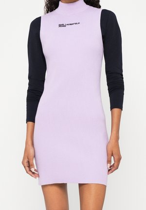 Femme portant une robe lilas sans manches côtelée sur un haut noir à manches longues avec le texte "KARL LAGERFELD JEANS" sur la poitrine.