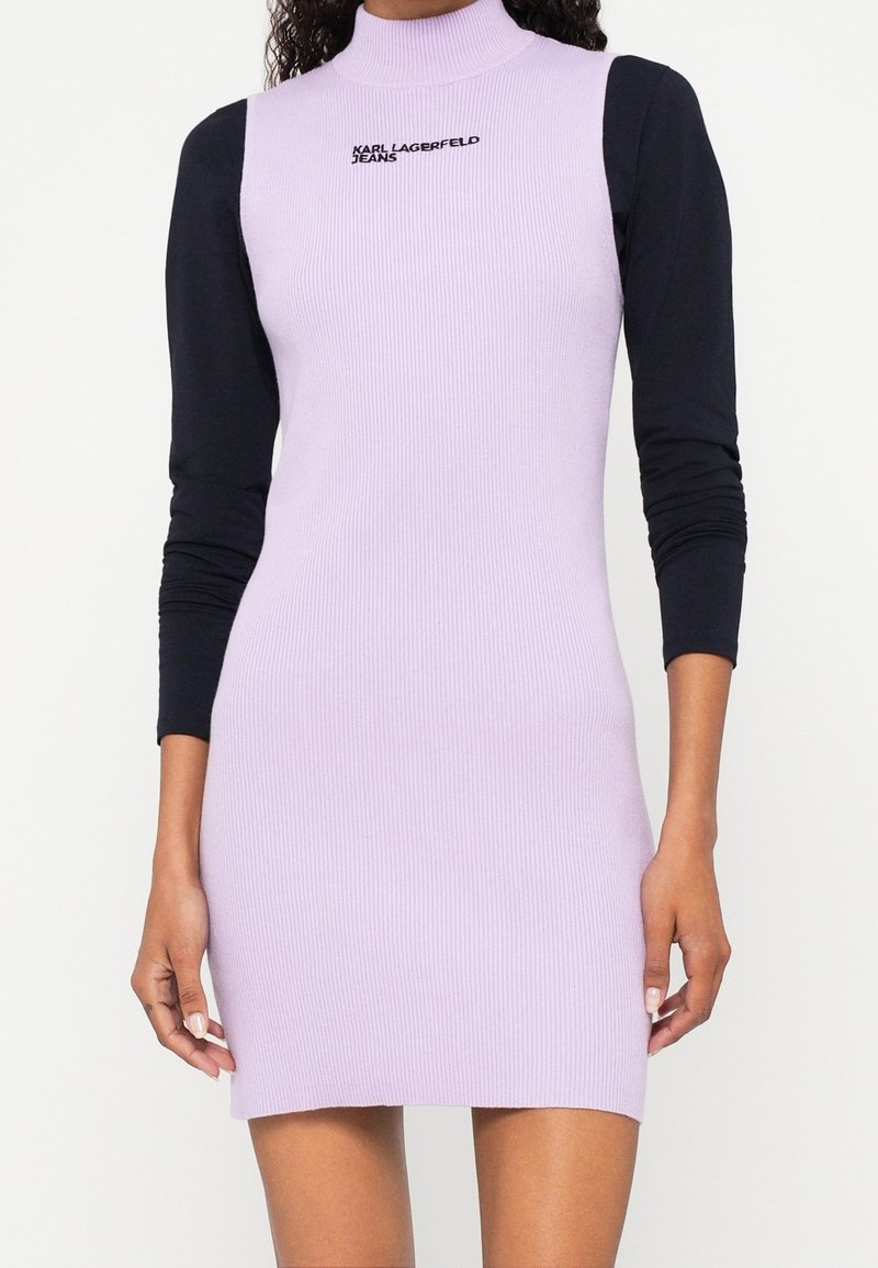 Femme portant une robe lilas sans manches côtelée sur un haut noir à manches longues avec le texte "KARL LAGERFELD JEANS" sur la poitrine.
