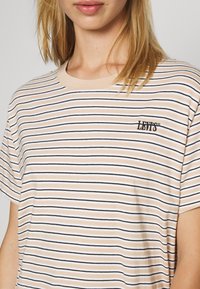 Różowa podkoszulka w paski, z krótkimi rękawami, z czarno-białymi poziomymi liniami oraz małym czarnym logo "LEVIS" na piersi.