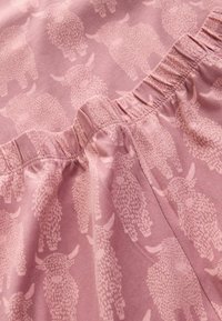 Zacht roze stof met lichtroze buffelpatronen en details van een elastische tailleband, waarbij de textuur en stikwerk op de stof zichtbaar zijn.