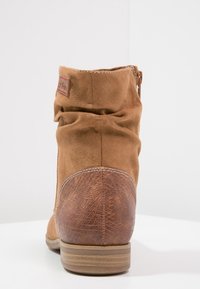 Braune Wildleder-Stiefelette mit einem gerafften Schaft, einem texturierten braunen Lederabsatz und einem seitlichen Reißverschluss. Sie verfügt über eine glatte Sohle und dezente Nähte.