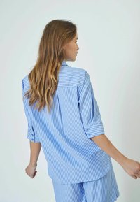 Light blue striped shirt, buttoned cuffs, loose fit, back view, smooth texture, designed with a pointed collar and shoulder yoke.