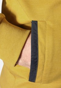 Gelbes Sweatshirt mit gerippten Bündchen; verfügt über eine Seitentasche mit einem Detail in Marineblau. Weicher Stoff, glatte Textur und lässiges Design.