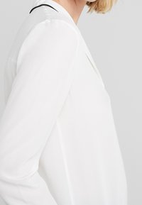 Witte blouse met lange mouwen, een gladde textuur en een subtiele zwarte accent langs de halslijn. Getailleerde pasvorm met een klassiek ontwerp.