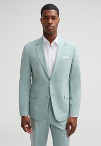 Light green suit with a textured finish, featuring a two-button closure, notched lapels, and side pockets. White shirt underneath.
