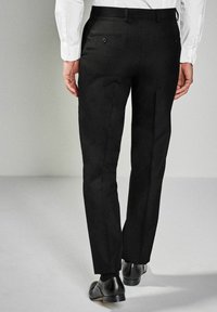Schwarze Hose mit geradem Schnitt, ausgestattet mit zwei Gesäßtaschen und sauberem Finish. Kombiniert mit einem weißen Langarmhemd und schwarzen Schuhen.