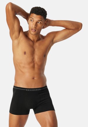 Schwarze Boxershorts mit einem weichen Bund, auf dem der Markenname "SCHIESSER" in Grau zu sehen ist. Der Stoff wirkt glatt und eng anliegend.