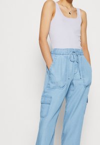 Light blue, lightweight cargo pants with an elastic waistband, front pockets, and drawstring detail. Features a relaxed fit and stitched accents.