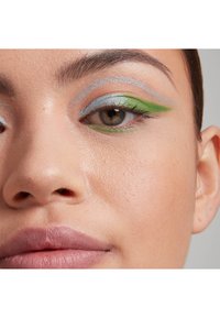 Primo piano di un volto con ombretto argento e verde scintillante, texture della pelle liscia e labbra nude sottili.