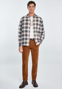 Mėlyna, smėlio ir oranžinė plaid flanelinė marška, dėvima ant kreminės spalvos marškinėlių. Rudos aksominės kelnės ir rudi raištiniai batai eina kartu su apranga.