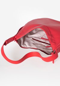 Rode leren tas met een enkele schouderband. Interieur met beige stoffen voering met geometrisch patroon en vakken voor organisatie. Ritssluiting.