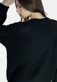 Schwarzer Strickpullover mit lässiger Passform, gerippter Textur und weiten Ärmeln. Der Rücken hat einen einfachen, rund geschnittenen Ausschnitt.